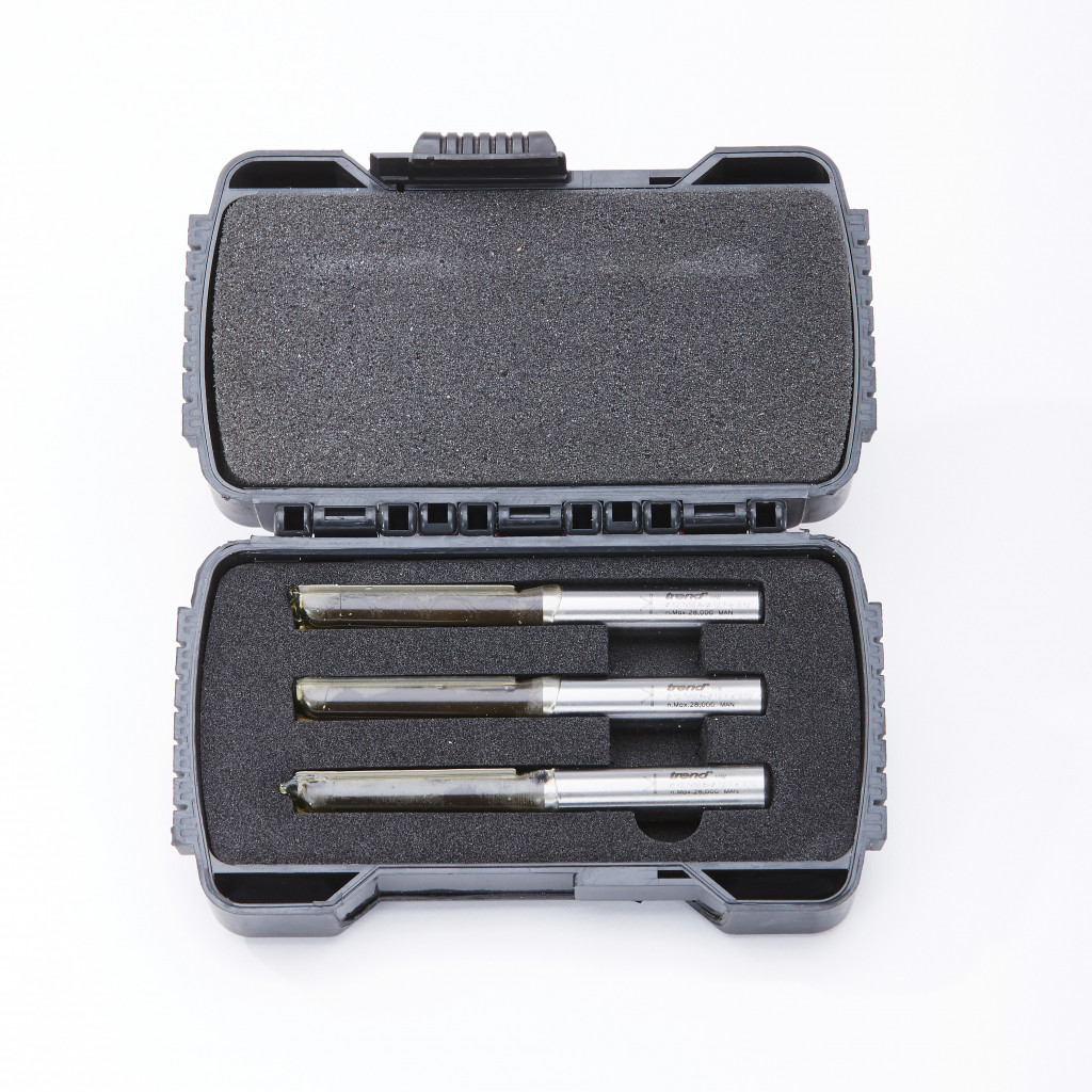 A black plastic case with foam padding holds three silver drill bits arranged in a row. The case is open and the drill bits are neatly secured in individual slots. The background is white.,