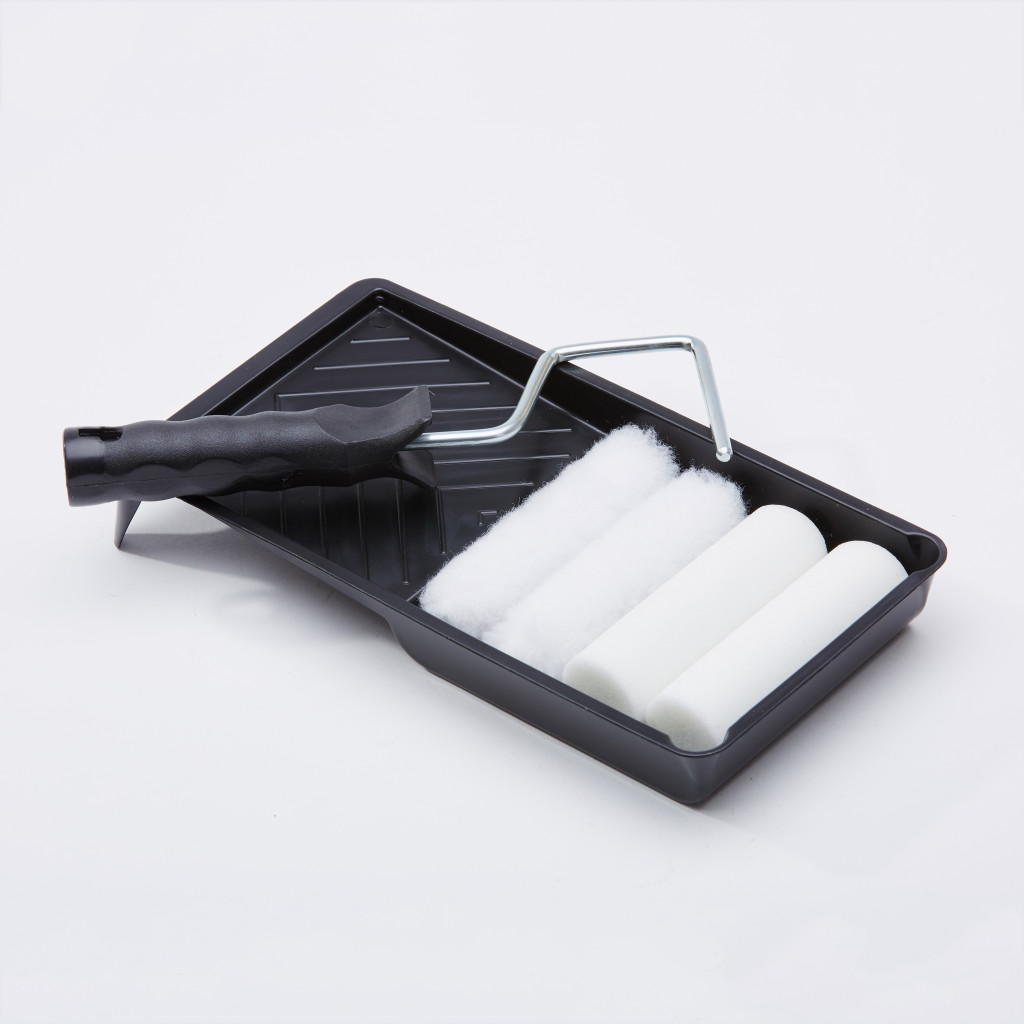 A black paint tray holds a paint roller with a black handle and three extra white foam roller covers, all set against a plain white background.