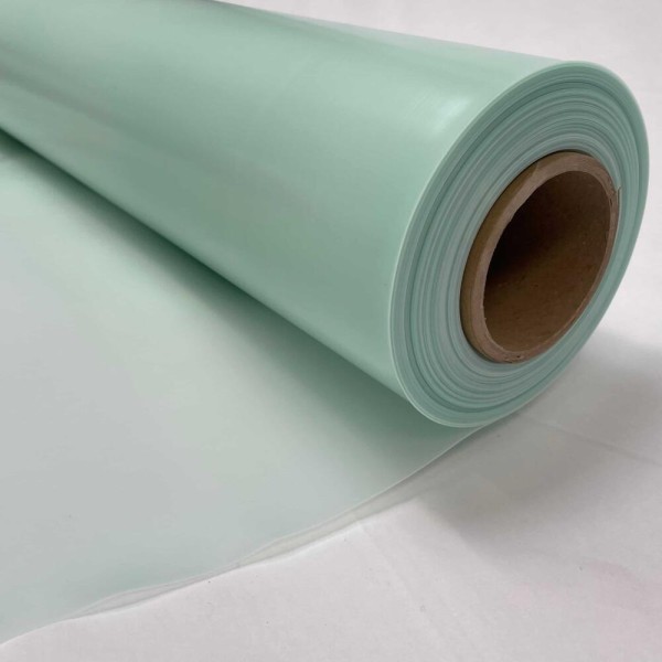 A close-up of a large roll of light green plastic or vinyl sheet material, partially unrolled on a white surface.