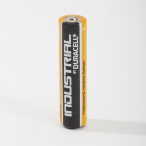 A single AA Duracell Industrial alkaline battery stands upright on a white surface, showing black and orange casing with white text.
