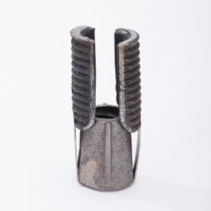 A metallic, cylindrical object with a textured surface and two ribbed, upright prongs, standing on a white background. The metal shows signs of wear and rust.