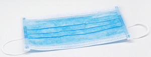 A blue disposable surgical face mask with white ear loops, lying flat on a white surface.