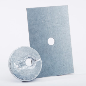A rectangular metal plate with a circular hole stands upright behind a round metallic object, also with a hole and an indented groove, both placed on a white background.