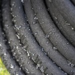 Close-up of a black garden soaker hose coiled in a spiral, with water droplets visible on its textured surface.