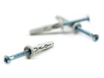 Close-up of two gray plastic wall plugs with metal screws, one in sharp focus in the foreground and the other out of focus in the background, set against a white surface.
