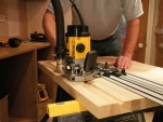 A yellow and black DEWALT plunge router with a fine depth adjuster and a guide fence, for cutting grooves, rebates, and profiles in timber.
