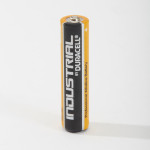 A single AA Duracell Industrial alkaline battery stands upright on a white surface, showing black and orange casing with white text.