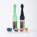 Two Markman marking tools, one green (standard) and one black (deep hole), stand upright. In front of them are four circular colored components: blue, brown, yellow, and red, resting on a white surface.