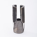 A metallic, cylindrical object with a textured surface and two ribbed, upright prongs, standing on a white background. The metal shows signs of wear and rust.