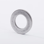 A metallic washer standing upright on a white surface, with a circular hole in the center and a slightly textured, silver-gray finish.