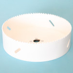 A white circular hole saw drill bit with sharp teeth along the edge and several elongated holes in the side, placed on a light blue background.