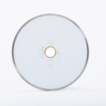 A round ceramic cutting blade with a metallic edge and a central hole, displayed upright against a plain white background. Text and small symbols are printed in the center of the blade.