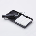 A black paint tray holds a paint roller with a black handle and three extra white foam roller covers, all set against a plain white background.