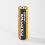 A single Duracell Industrial professional alkaline AA battery stands upright on a white surface, showing its black and orange label with the positive terminal visible on top.