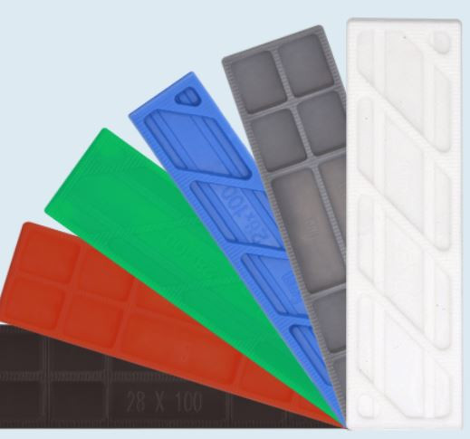 Six rectangular, plastic measuring or calibration strips in different colors (black, red, green, blue, gray, and white) are arranged in a fan shape against a light background.