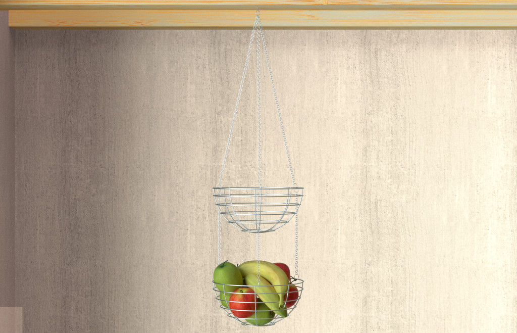 A metal hanging basket with two tiers is attached to a wooden shelf. The lower basket contains apples and bananas, while the upper basket is empty. The background is a light, textured wall.