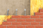 A cross-section illustration showing red brick masonry with yellow insulation behind, metal brackets anchoring to a concrete wall, and circular spacers between the layers.