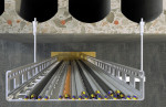 Overhead view of multiple cables organized in a metal cable tray, mounted against a wall with a stone and concrete finish above and a wooden floor below.