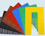 A set of six rectangular plastic boards in black, brown, red, blue, green, and yellow, fanned out on a light background. Each board has a grid of raised rectangles.