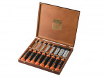 A wooden box containing a set of six Bahco chisels with black and orange handles, neatly arranged side by side with blade guards on some chisels. The box lid is open.