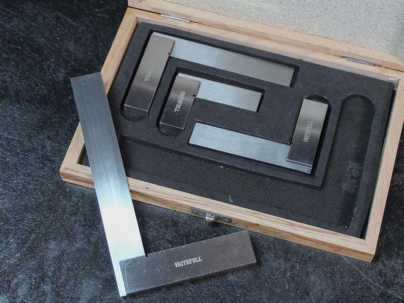 A wooden case with foam lining holds four metal engineer’s squares of varying sizes, one of which is placed outside the case on a dark surface. The squares are labeled RUITOOL.