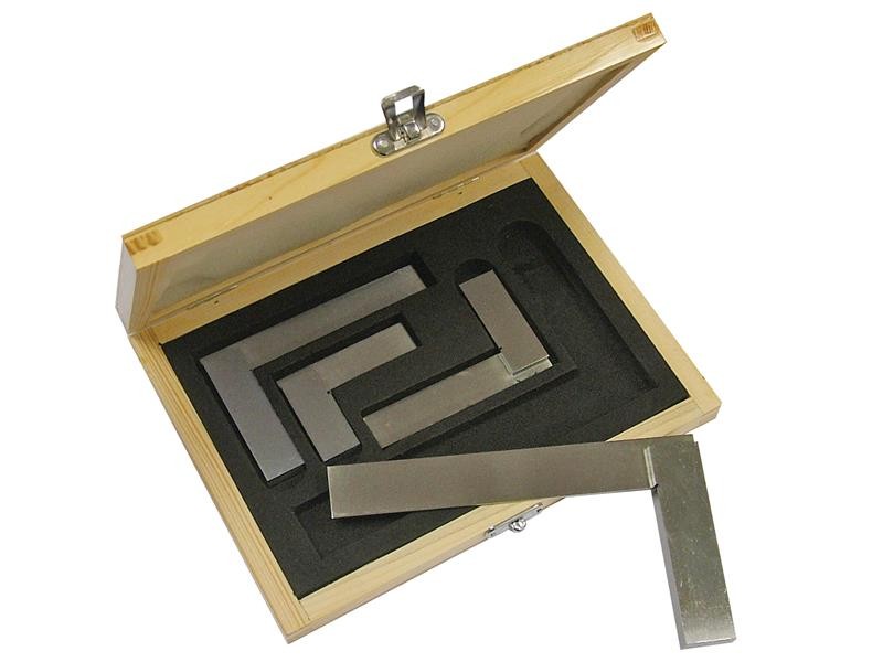 A wooden box with a hinged lid contains four metal engineers squares of different sizes, neatly arranged in black foam cutouts. One square rests outside its slot on top of the foam.