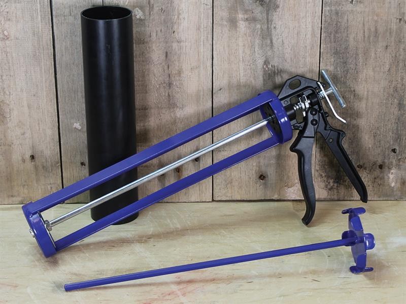 A purple caulking gun with a black handle is lying on a wooden surface next to a black cylindrical tube and a long, thin rod with a handle, all set against a wooden plank background.