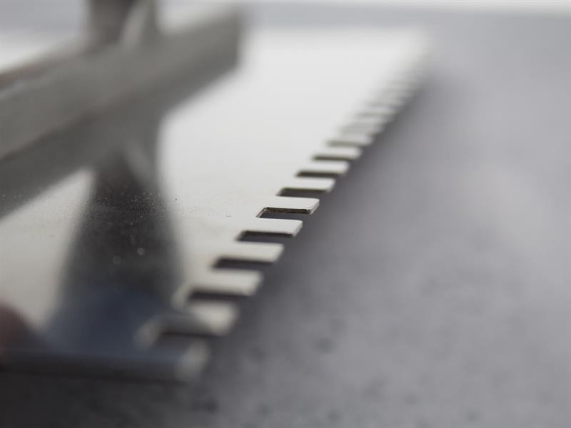 A Faithfull notched tile trowel with 115mm notches for combing adhesive on floors and walls, ensuring even coverage beneath tiles.