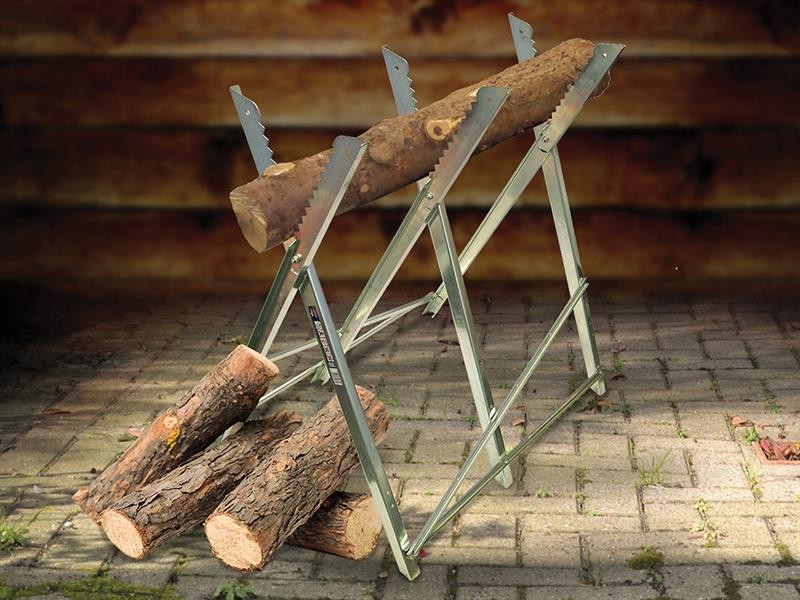 A metal sawhorse holds a large log, with several cut logs lying on the ground beneath it. The scene is set on a stone-paved surface with a wooden wall in the background.