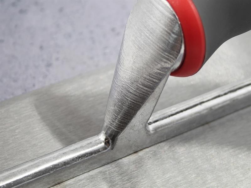 Close-up of a metal trowel with a red and gray handle on a smooth gray surface, showing the tools texture and fine details.