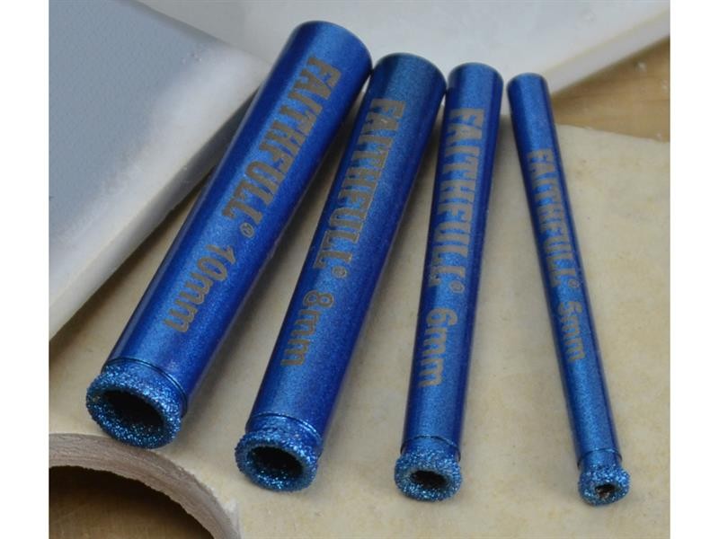 Four blue Faithfull diamond drill bits of varying diameters (10mm, 8mm, 6mm, 5mm) lying on a light surface, with textured tips for cutting through hard materials.