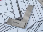 A metal engineering square labeled FAITHFULL rests on top of technical architectural blueprints with detailed measurements and lines.,