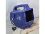A blue, plastic, hand-cranked flicker machine with a handle and a wheel, used for simulating movement or flutter effects, sits on a light surface next to a beige fabric.
