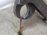 A close-up of a metal tool gripping the head of a rusty nail, partially embedded in a wooden surface, as the tool attempts to pull the nail out.