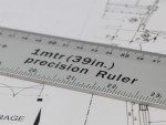 A close-up of a silver precision ruler labeled 1mtr (39in.) precision Ruler placed on top of technical drawings with measurement markings and diagrams visible underneath.,