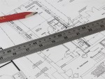 A close-up of architectural blueprints with a red pencil and a metal ruler placed on top, showing measurements and technical drawings of building plans.