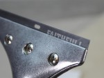 Close-up of a metal scraper with three screws and the word FAITHFULL partially visible on the blade. The background is blurred.,