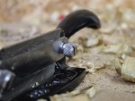A close-up of a metal hand plane tool resting on a workbench, surrounded by wood shavings. The focus is on the adjustment knob and handle of the tool.
