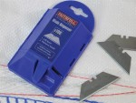 A blue Faithfull blade dispenser with two loose utility blades beside it, placed on a white textured surface with blue and red stitching. The dispenser’s instructions and branding are visible.