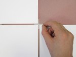 A hand places a white tile spacer between four white tiles, which are being installed over a pinkish surface.